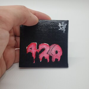 May include: A small black canvas painting with a pink dripping word "420" and a white signature in the top right corner.