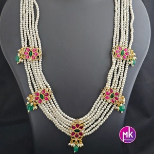 May include: A six-strand pearl necklace with pink and green floral accents. The necklace has five decorative pendants with pink and green stones. The necklace is paired with matching earrings.