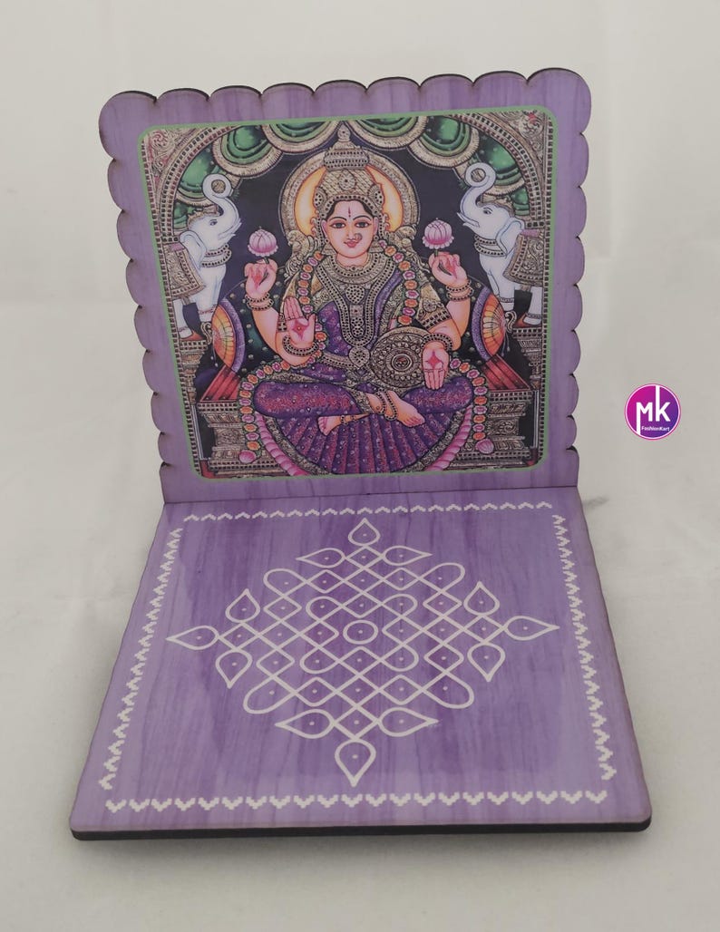 May include: A purple wooden folding stand featuring a printed illustration of a deity seated between two elephants on the upright panel and a white geometric kolam pattern on the base. The edges of the stand have a scalloped design.