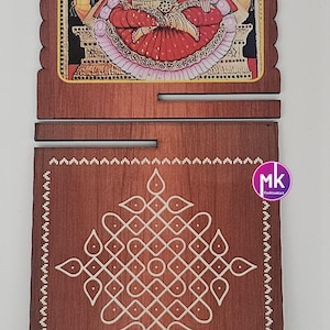 May include: A two-piece wooden plaque set featuring a top piece with a colorful illustration of a deity flanked by elephants and a bottom piece with a white geometric kolam pattern. A metal ruler shows the width is approximately 4.5 inches.