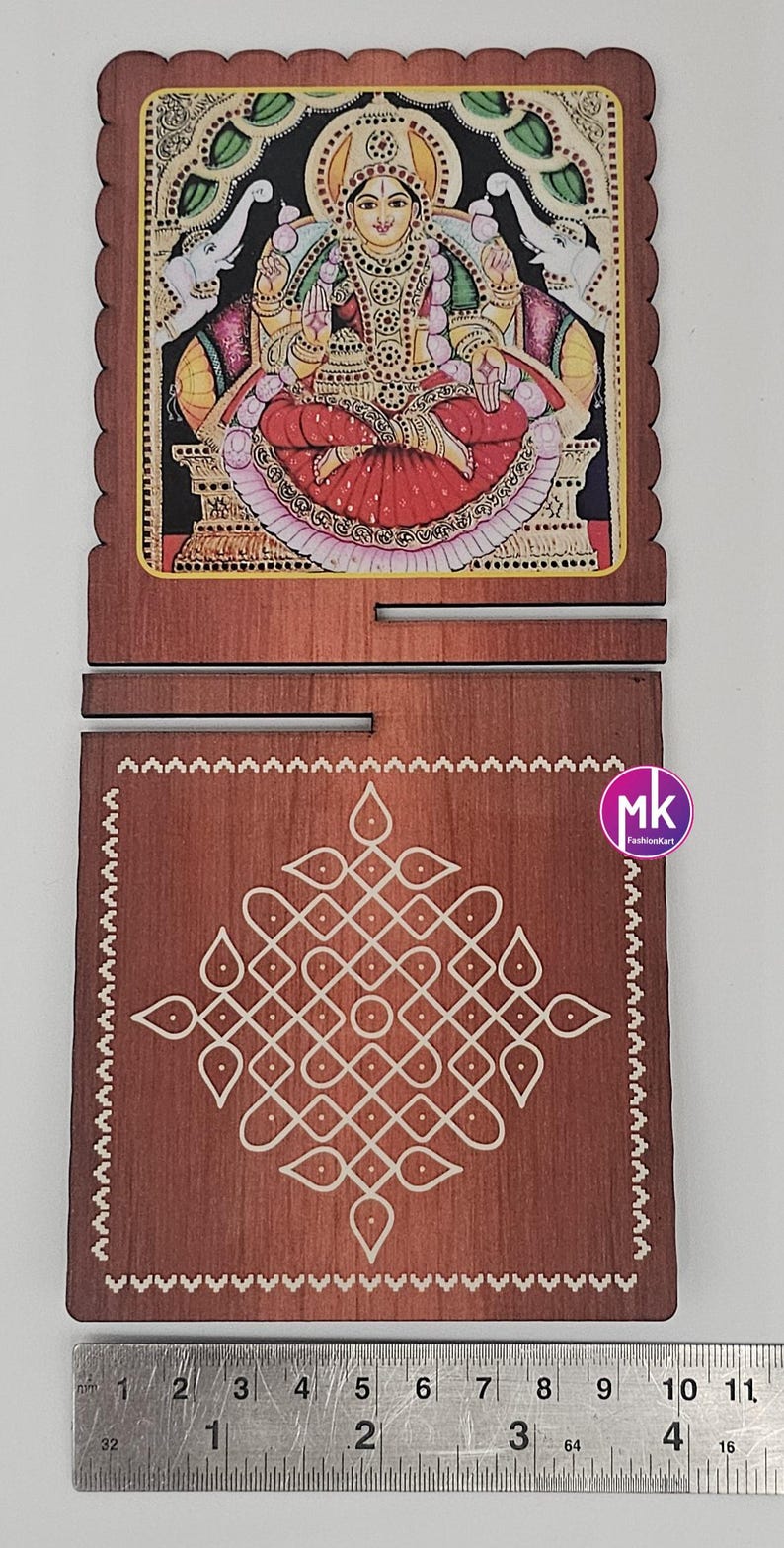 May include: A two-piece wooden plaque set featuring a top piece with a colorful illustration of a deity flanked by elephants and a bottom piece with a white geometric kolam pattern. A metal ruler shows the width is approximately 4.5 inches.