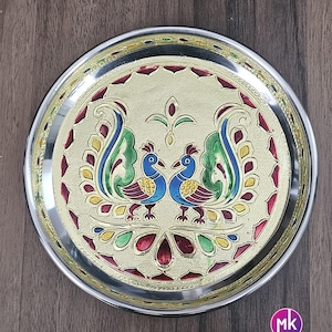 May include: A silver serving plate with a gold rim and a colorful peacock design. The plate features two peacocks facing each other with their tails spread out. The design is intricate and detailed, with a variety of colors including red, blue, green, and yellow.