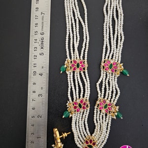 May include: A multi-strand pearl necklace with gold and pink flower accents. The necklace has five strands of pearls and three gold flower accents with pink and green stones. The necklace is paired with matching earrings.