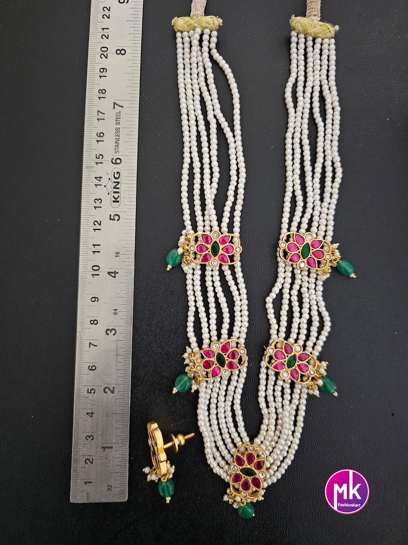 May include: A multi-strand pearl necklace with gold and pink flower accents. The necklace has five strands of pearls and three gold flower accents with pink and green stones. The necklace is paired with matching earrings.
