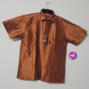 May include: A brown short-sleeved button-down shirt made of silk. The shirt has a collar and a pocket on the left side. The shirt has a tag that says "Silk Line".
