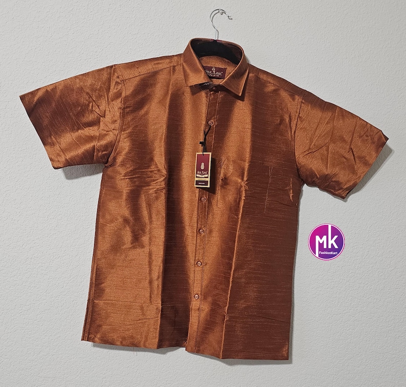 May include: A brown short-sleeved button-down shirt made of silk. The shirt has a collar and a pocket on the left side. The shirt has a tag that says "Silk Line".