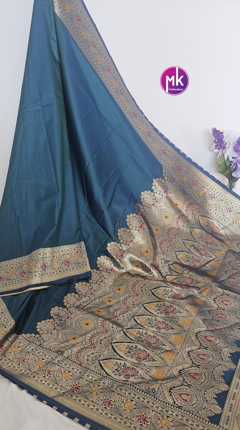 Puede incluir: Un sari de seda azul turquesa con un borde dorado y negro. El sari tiene un dise&ntilde;o tradicional indio con intrincados patrones florales y motivos paisley.