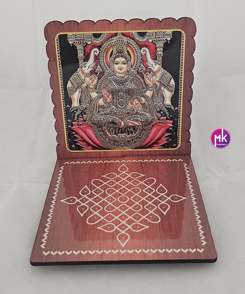 May include: A wooden folding stand with a scalloped edge featuring a colorful illustration of a deity seated on a lotus flower flanked by two elephants. The base displays a white geometric kolam pattern on a brown wood-grain surface.