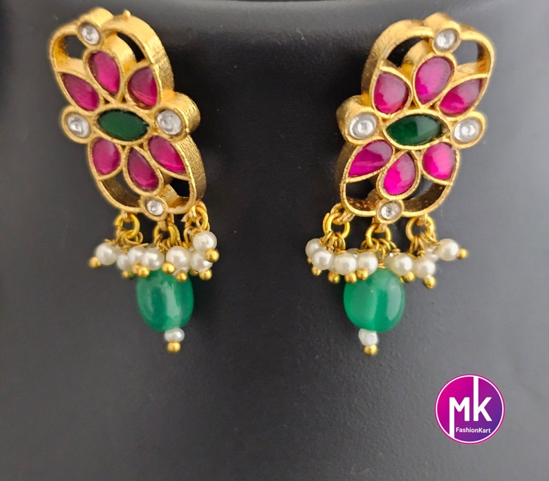 May include: A pair of gold earrings with pink and green stones, and white pearl accents. The earrings feature a floral design.