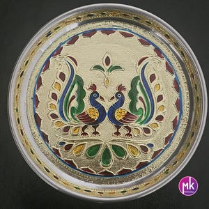 May include: A silver round serving tray with a gold rim and a peacock design in the center. The peacock design is in shades of blue, green, red, and yellow.
