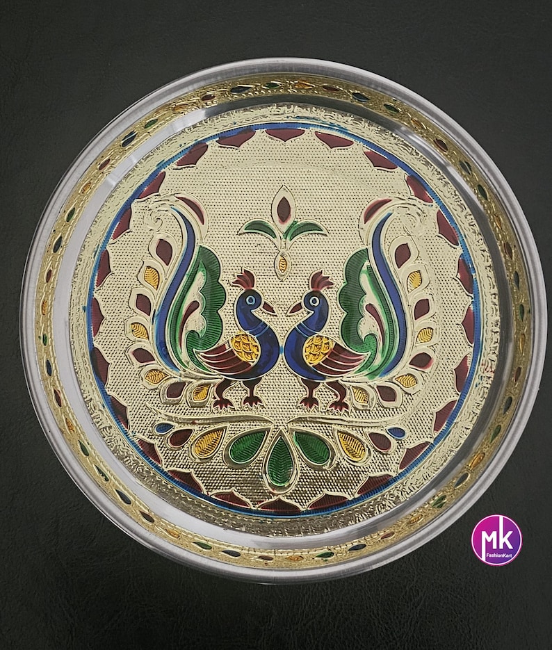 May include: A silver round serving tray with a gold rim and a peacock design in the center. The peacock design is in shades of blue, green, red, and yellow.