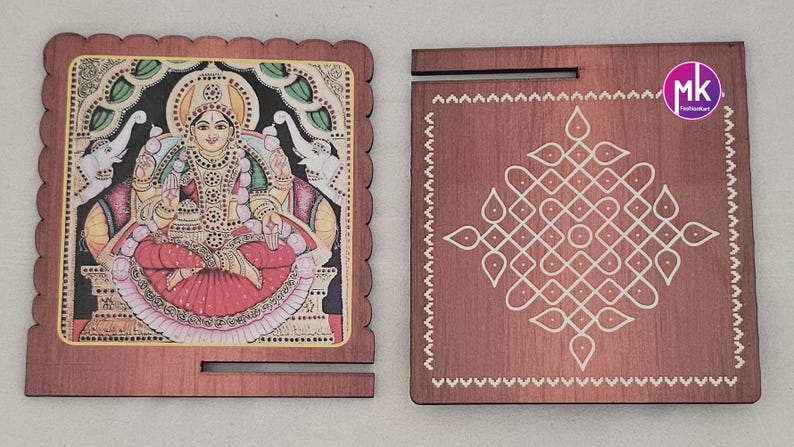 May include: Two square wooden plaques with a dark brown finish. The left plaque features a colorful illustration of a seated deity flanked by two elephants. The right plaque displays a white geometric kolam pattern and a circular mk logo.