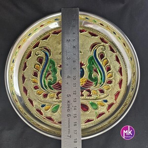 May include: A silver serving plate with a gold rim and a peacock design. The peacock is painted in shades of green, red, yellow, and blue. The plate is 7 inches in diameter.