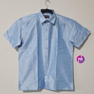 May include: A light blue short-sleeved button-down shirt with a pocket on the left side. The shirt is made of a silky material and has a subtle sheen.