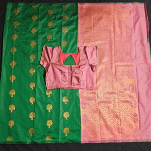 May include: A green and pink silk sari with a gold tree pattern. The sari is paired with a pink blouse.