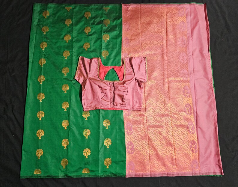 May include: A green and pink silk sari with a gold tree pattern. The sari is paired with a pink blouse.