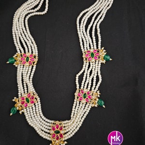 May include: A six-strand pearl necklace with gold and pink floral accents. Each floral accent has a green gemstone in the center.