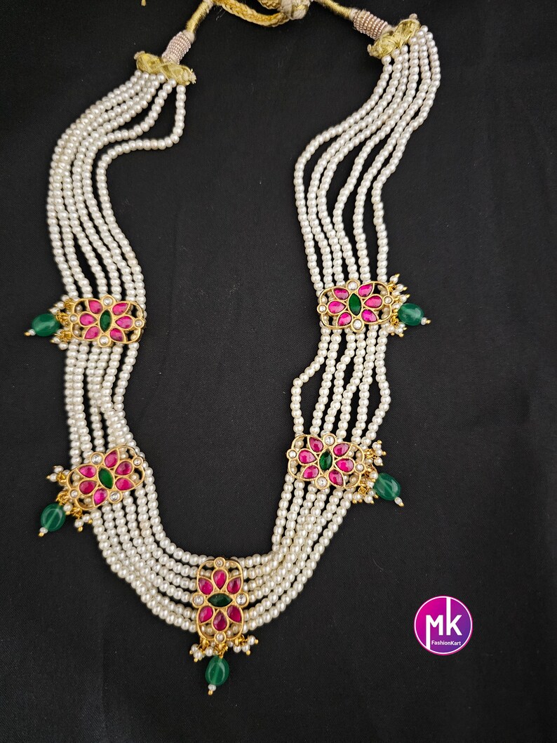 May include: A six-strand pearl necklace with gold and pink floral accents. Each floral accent has a green gemstone in the center.
