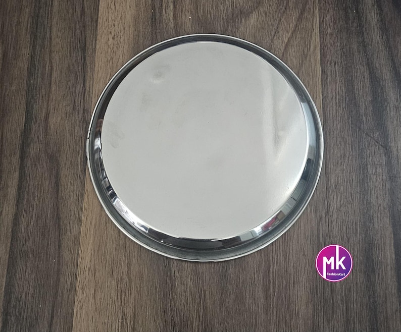 May include: A round, silver serving tray with a smooth, reflective surface. The tray is made of stainless steel and has a slightly raised rim.