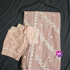 May include: A light pink sheer saree with silver sequins and floral embroidery. The saree is paired with a matching sleeveless blouse.