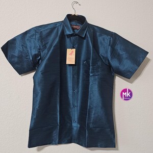 May include: A teal blue short-sleeved button-down shirt with a pocket on the left side. The shirt has a woven texture and is hanging on a hanger. The brand label says "Axxia".