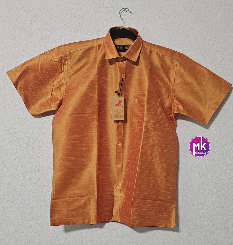 May include: A short-sleeved, gold-colored button-down shirt with a pocket on the left chest. The shirt has a subtle sheen and a textured fabric. The brand name "Azotice" is visible on the tag.