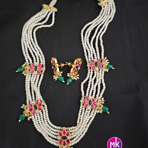 May include: A multi-strand pearl necklace with pink and green gemstone flower accents. The necklace is paired with matching earrings. The necklace has a gold chain and a tassel.