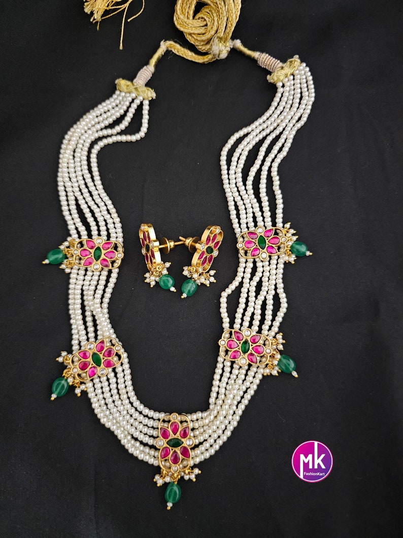 May include: A multi-strand pearl necklace with pink and green gemstone flower accents. The necklace is paired with matching earrings. The necklace has a gold chain and a tassel.