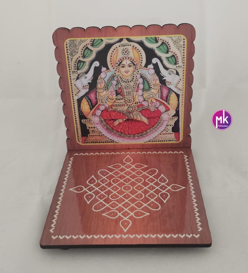 May include: A wooden folding stand with a scalloped edge, featuring a colorful illustration of a deity seated on a throne with two elephants on the sides. The base displays a white geometric kolam pattern on a polished brown wood surface.