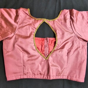 May include: A maroon satin blouse with a keyhole back and gold trim. The trim is embellished with small rhinestones.