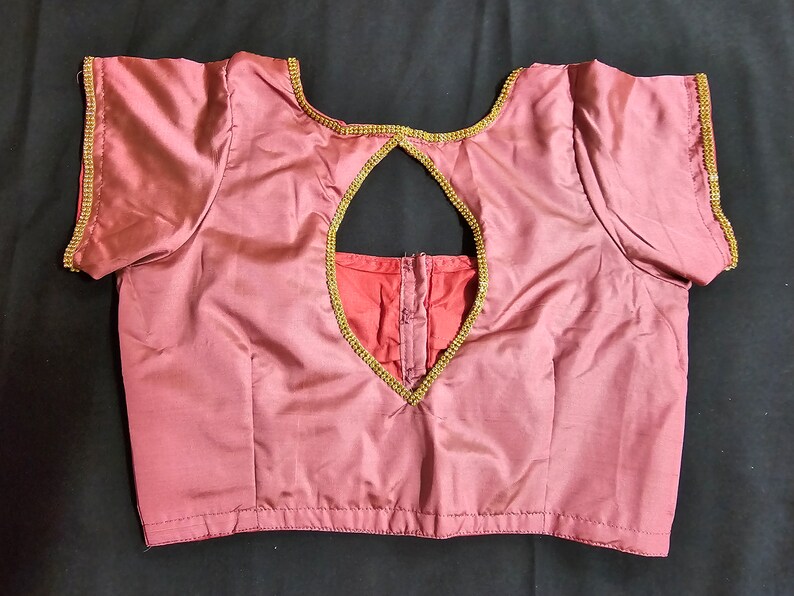 May include: A maroon satin blouse with a keyhole back and gold trim. The trim is embellished with small rhinestones.