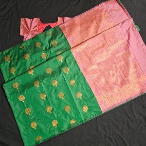 May include: A green and pink silk saree with a gold tree pattern. The saree has a pink border with a gold design.