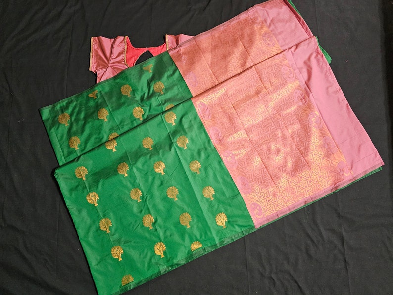 May include: A green and pink silk saree with a gold tree pattern. The saree has a pink border with a gold design.