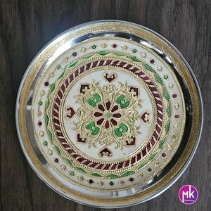 May include: A silver round serving tray with a white center and intricate gold and green floral design. The design includes red accents and a gold rim.