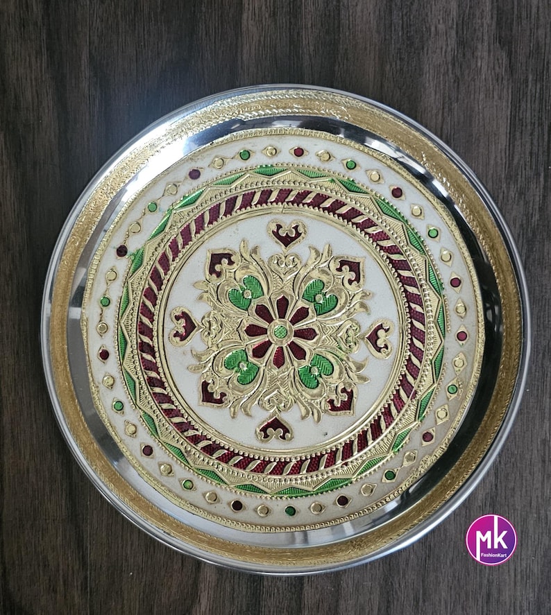 May include: A silver round serving tray with a white center and intricate gold and green floral design. The design includes red accents and a gold rim.