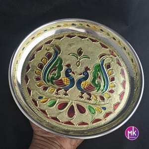 May include: A silver serving plate with a gold background and a colorful peacock design. The plate has a raised rim and a decorative border.