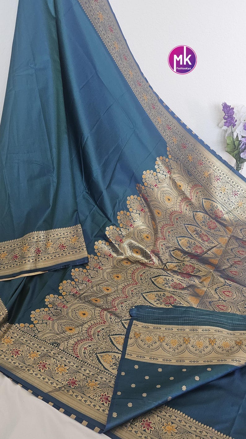 Puede incluir: Un sari de seda azul turquesa con un borde dorado y negro. El borde presenta intrincados dise&ntilde;os florales y paisley. El sari tiene un patr&oacute;n tejido de peque&ntilde;os puntos en el pallu.