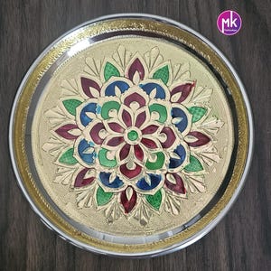 May include: A round, gold-colored metal serving tray with a decorative, multi-colored floral design in the center. The tray has a silver rim.