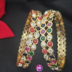 May include: A set of four gold bangles with colorful stones and white pearls. The bangles are stacked on top of each other and have a shiny finish.