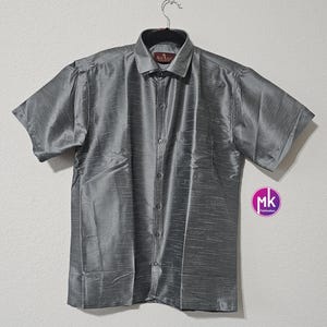 May include: A gray short-sleeved button-down shirt with a subtle sheen. The shirt has a pocket on the left side and a button-up collar.