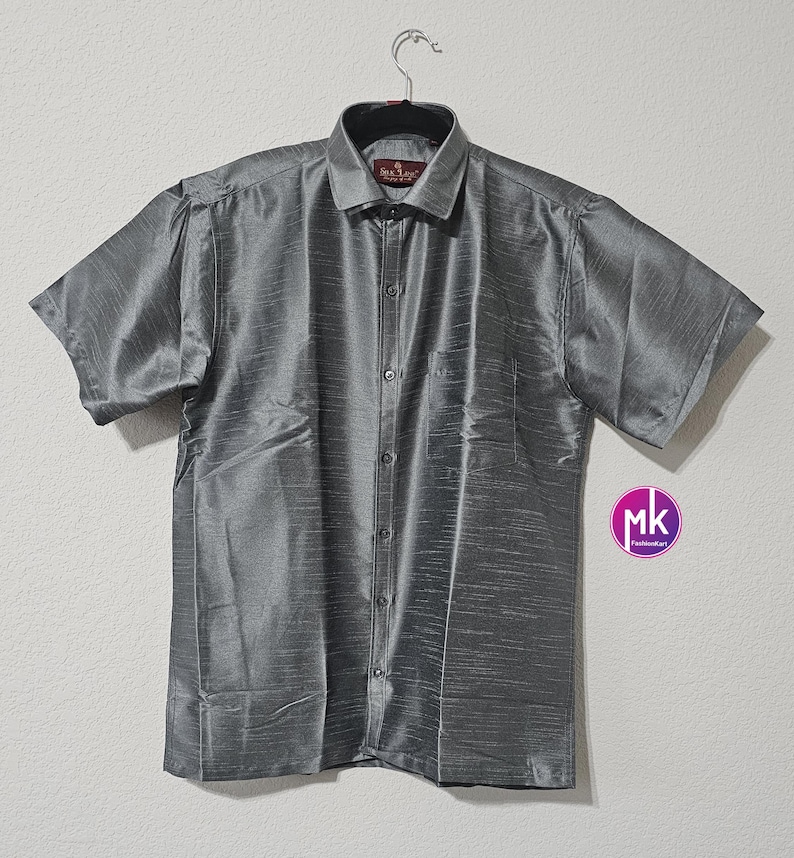 May include: A gray short-sleeved button-down shirt with a subtle sheen. The shirt has a pocket on the left side and a button-up collar.