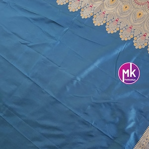 Puede incluir: Un sari de seda azul turquesa con un borde bordado en oro y rojo. El borde presenta un dise&ntilde;o de cachemira con acentos florales. El sari es una prenda tradicional india.