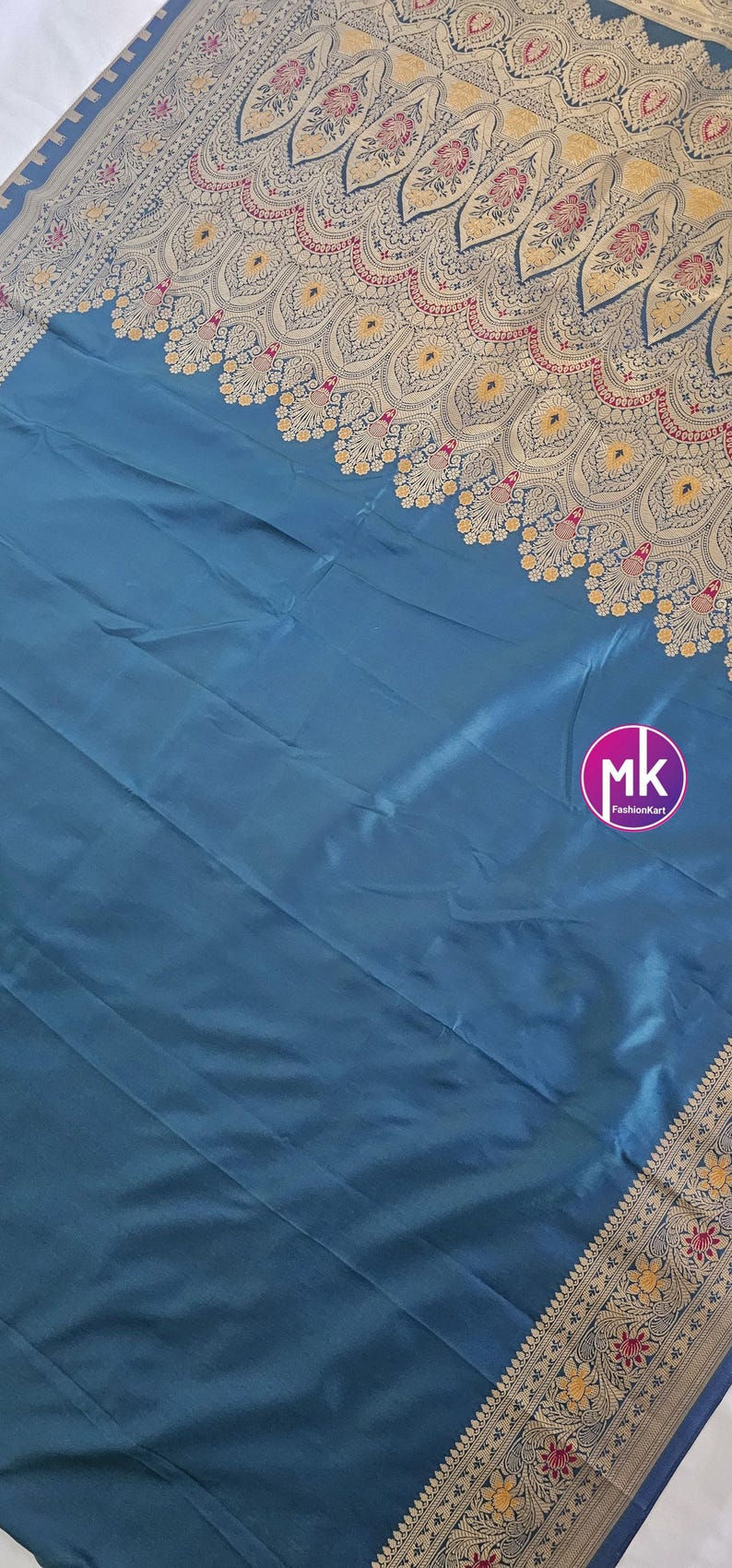 Puede incluir: Un sari de seda azul turquesa con un borde bordado en oro y rojo. El borde presenta un dise&ntilde;o de cachemira con acentos florales. El sari es una prenda tradicional india.