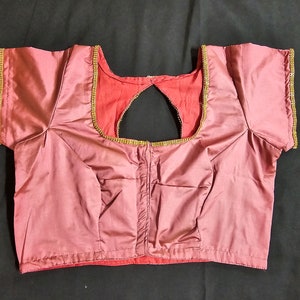May include: A mauve satin blouse with a keyhole back and gold trim around the neckline and sleeves.