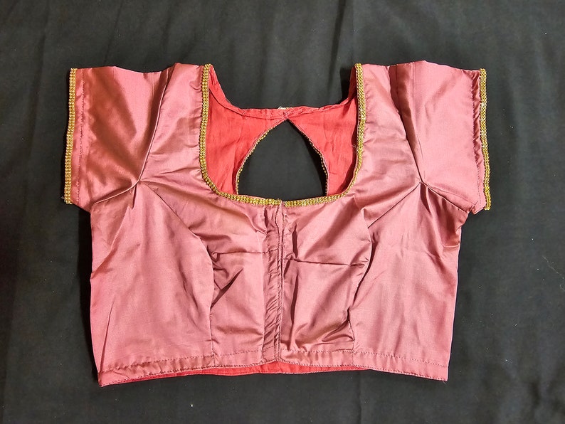 May include: A mauve satin blouse with a keyhole back and gold trim around the neckline and sleeves.