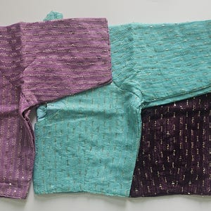 May include: Four embroidered blouses in shades of purple, teal, and dark purple. The blouses have short sleeves and intricate patterns. One blouse has tie-up straps. The logo "MK Fashion Mart" is in the bottom right corner.