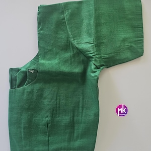 May include: A vivid green blouse with short sleeves. The garment has a tailored fit, with visible seams and a button closure. The fabric has a subtle sheen, suggesting a silk or satin material. The blouse is displayed on a plain white background.