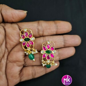 May include: A pair of gold earrings with pink and green stones. The earrings have a floral design and are hanging from a chain with small white beads.