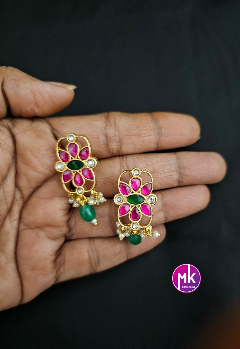May include: A pair of gold earrings with pink and green stones. The earrings have a floral design and are hanging from a chain with small white beads.