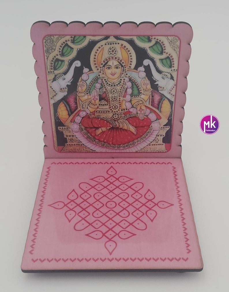 May include: A pink wooden folding stand featuring a scalloped edge. The upright panel displays a colorful illustration of a deity seated on a throne with two elephants. The base panel features a symmetrical pink geometric kolam pattern design.